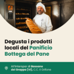 Il fornaio del Panificio Bottega del Pane in divisa bianca mostra una pagnotta appena sfornata davanti a un forno professionale. Evento di degustazione all'Interspar di Bassano del Grappa, C.C. Il Grifone.